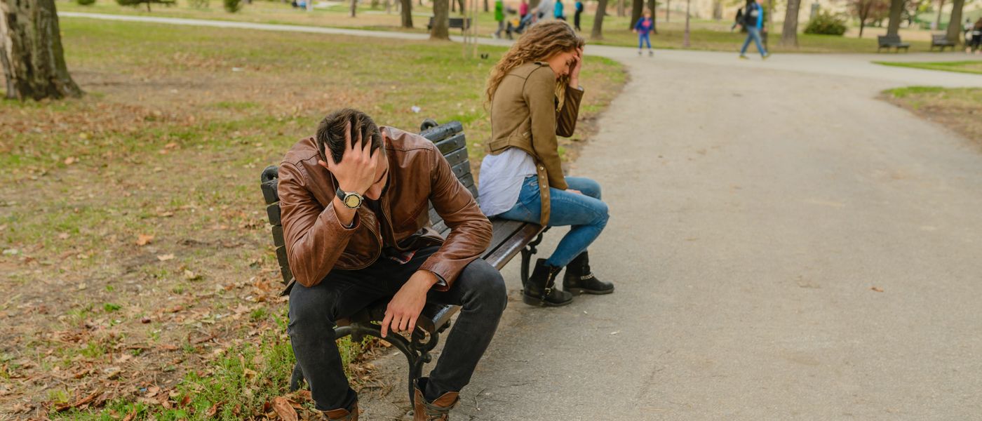 A man and a woman sitting apart on a park bench