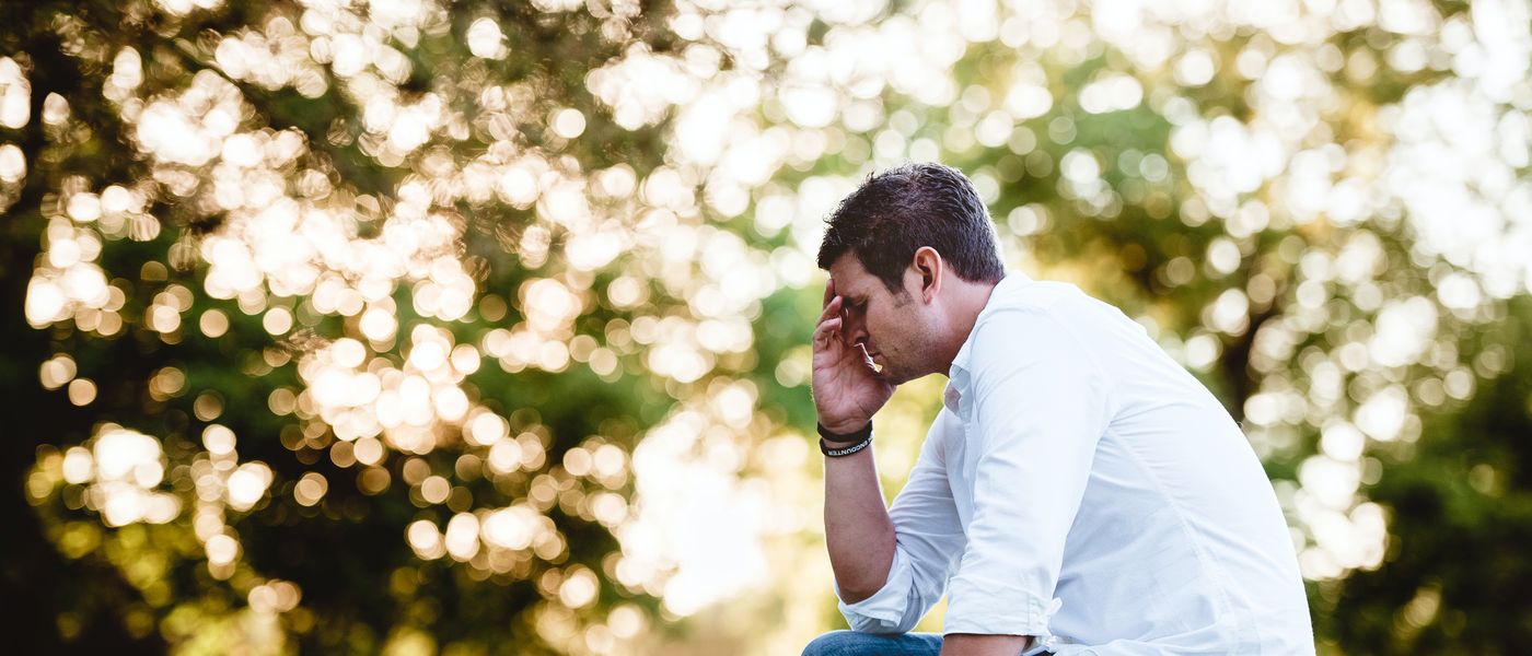 A man sitting outdoors with his hand to his head